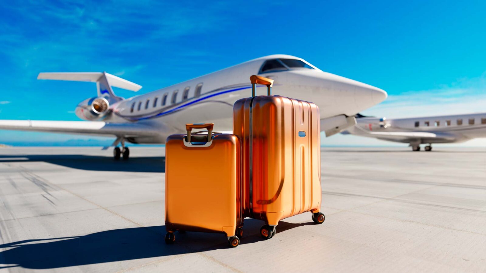 Due trolley rigidi color arancio metallizzato su pista d’aeroporto con jet privato sullo sfondo